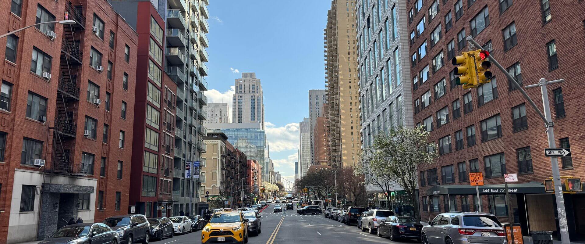 Looking down a wide Upper East Side avenue on a sunny day with yellow cabs and brick apartment buildings